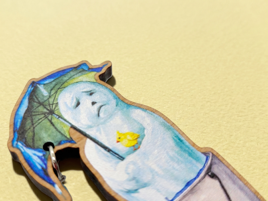 A 2.5 inch laser cut wooden brooch of a melting snowman holding and umbrella with a dangling blue glass bead raindrop and small yellow bird resting on his arm.