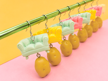 Several pairs of handmade Couch Potato earrings featuring couch charms with miniature potatoes dangling underneath.