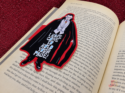 A Dracula magnetic bookmark securely clipped on the side pages of an open book. The classic horror vampire design features a black cape, red accents and original Junkyard Bunnie artwork.