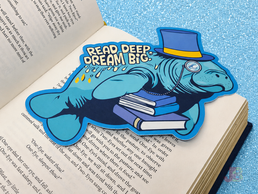 A close-up shot of a dapper manatee die-cut bookmark. The cute sea cow is holding a stack of books while wearing a top hat and monocle. The bookmark is 7 inches wide and double-sided.
