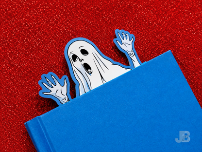 A lifestyle photo of the extra-large 7-inch ghost bookmark peeking out from the top pages of thick, hardcover novel.