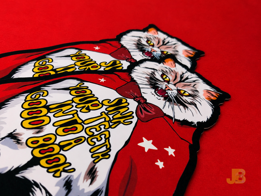 Die-cut bookmarks of a vampire Pallas cat in a red cape with the words "sink your teeth into a good book" on the front.