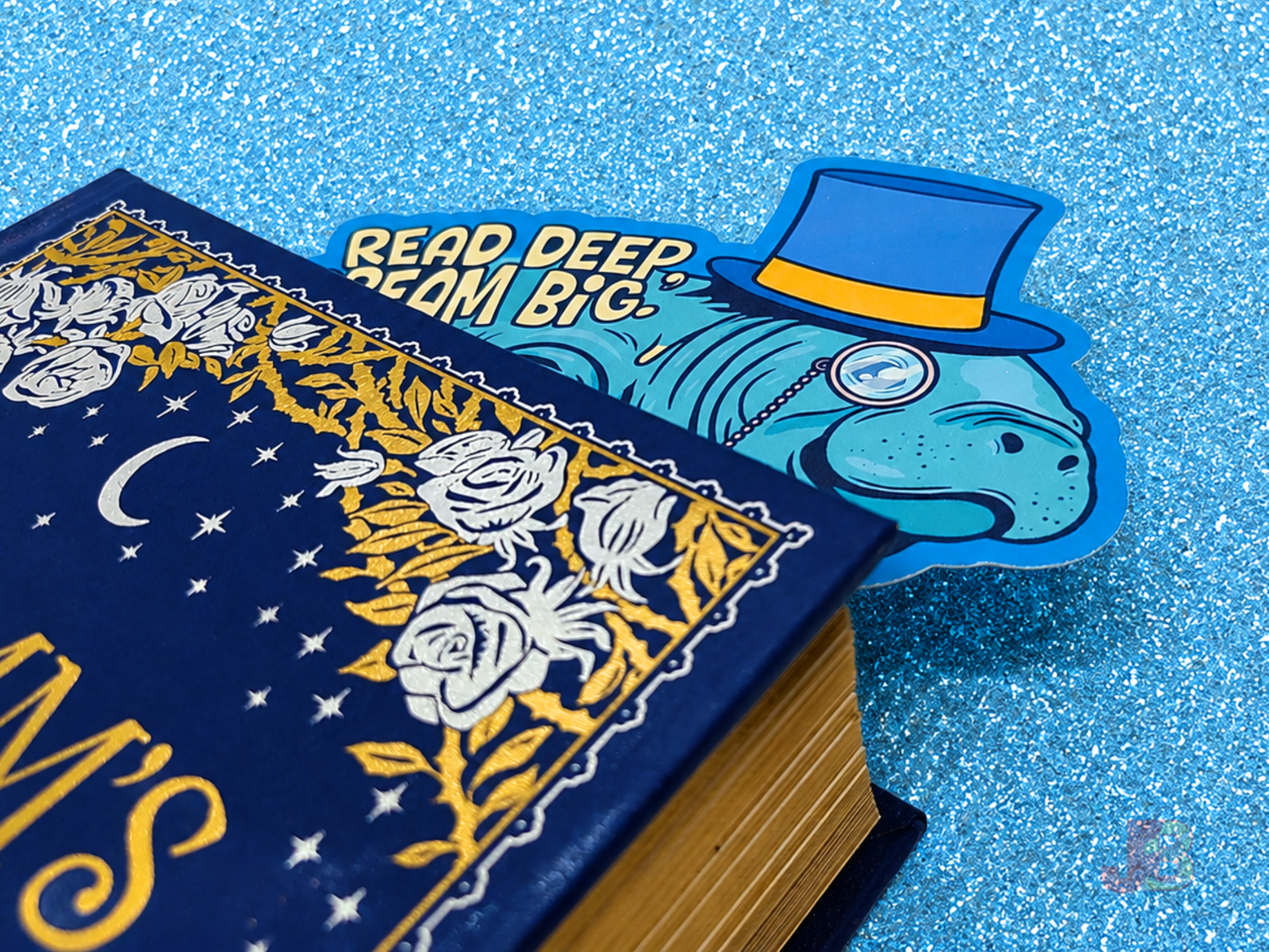 A cute ocean-themed accessory. The manatee bookmark is popping out the pages at the top of a hardcover novel and is double-sided and printed on premium cotton coverstock. It is the perfect gift for book lovers and marine biology fans.