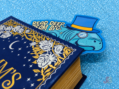 A cute ocean-themed accessory. The manatee bookmark is popping out the pages at the top of a hardcover novel and is double-sided and printed on premium cotton coverstock. It is the perfect gift for book lovers and marine biology fans.